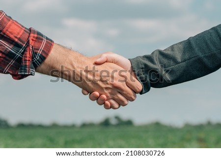 Mortgage loan officer and farmer shaking hands upon reaching an agreement for financial allowance application, banker and farm worker in corn maize crop field.