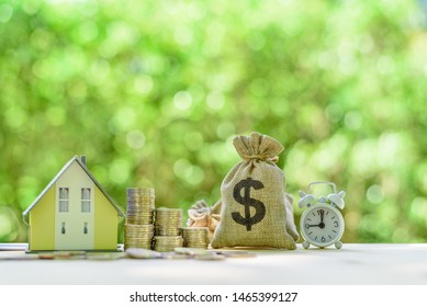 Mortgage-backed security MBS, financial concept : House model, stacks of rising coins, US dollar, money bags, a clock on a table over green background, depicts investment in home bought from the bank 