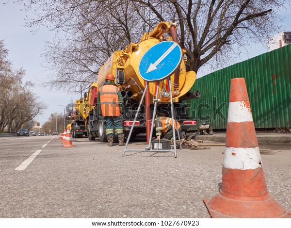 MOSCOW, APR.29, 2017: View on yellow city service\
Mosvodostok truck, workers, road signs safety cones. Road water\
drainage cleaning truck and equipment devices tools. Road drainage\
city service