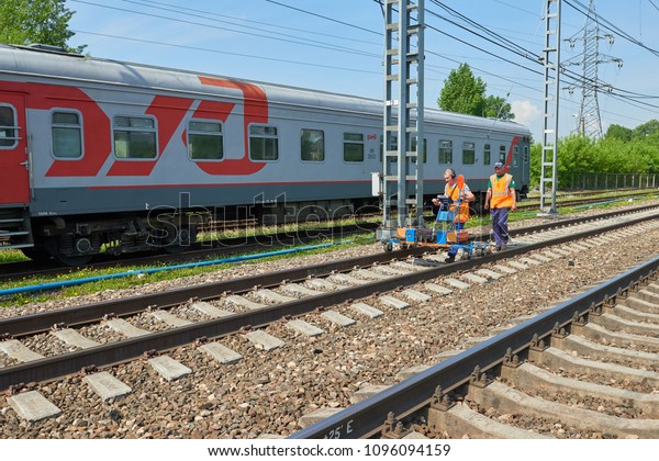 MOSCOW,\
MAY, 18, 2018: View of railway maintenance workes group with\
trolley doing rail tracks ultrasonic inspection and visual control\
and train cars in the background. People  at\
work