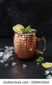 Moscow mule alcoholic cocktail in copper mug with crushed ice, mint and lemon over black stone background. Side view, close up, copy space