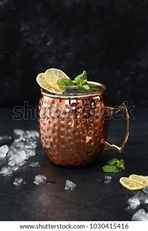 Moscow mule alcoholic cocktail in copper mug with crushed ice, mint and lemon over black stone background. Side view, close up, copy space