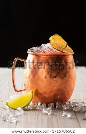 Moscow Mule cocktail in a Copper Mug garnished with dried Lime and ice on black background