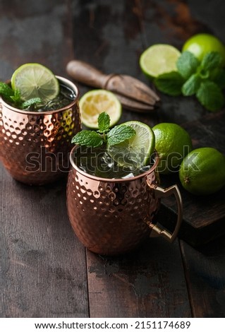 Moscow mule cocktail in a copper mug with lime and mint and wooden squeezer on dark wooden table background. 