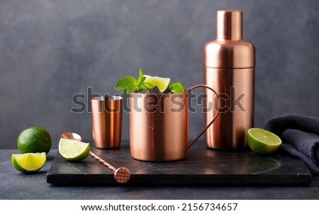 Moscow mule cocktail in copper mug, shaker with fresh mint, lime on marble board. Dark background. Copy space.