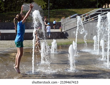 Moscow region, Russia, July 2021. A girl in wet clothes jumped up, stretching her arms up, catching the jets of the fountain. 