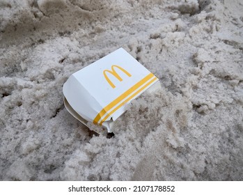 Moscow, Russia - 01.16.2022: McDonald’s Food Packaging In Dirty Snow On The Road. Fast Food, MacDonald’s Burgers. Disposable Hamburger Container. Dumped Hamburger Box. Environment Issues.