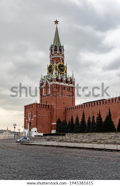 Moscow, Russia, 03.18.2021. Spasskaya\
Tower of the Moscow Kremlin with a clock and a ruby star on the\
spire in cloudy weather. A police car was parked\
nearby