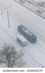 Moscow, Russia - 05-01-2022: Aerial View Of A Blue Public Transport Electric Bus That Stands At A Bus Stop During A Heavy Snow Storm In The Russian Capital. The Whole Wide Road Is Covered With Snow.