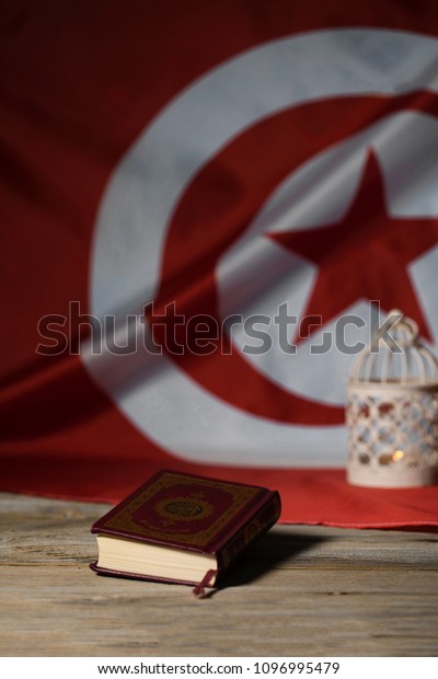 Moscow, Russia. 05/21/2018. Sacred book\
of Koran on a wooden surface. Tunisian flag in the background.\
Translation - the book contains verses of\
Koran