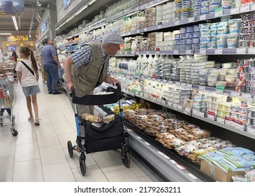 Moscow, Russia - 07.17.2022: Disabled Retired Elderly Man With A Walking Frame Looks With Surprise At Dairy Products In A Grocery Store. Milk, Food Price Increase, Hyperinflation And Inflation.