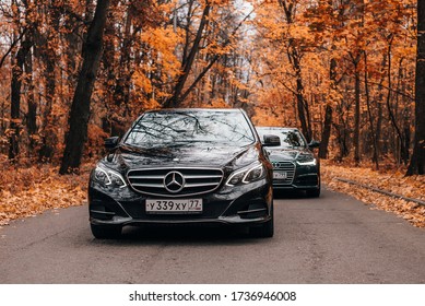 Moscow, Russia - 13 October 2019, Black Mercedes Benz E Class W212 And Black Audi A6 Parked In The Forest. Deep Autumn. Frontview. A Lot Of Fallen Orange Leaves.