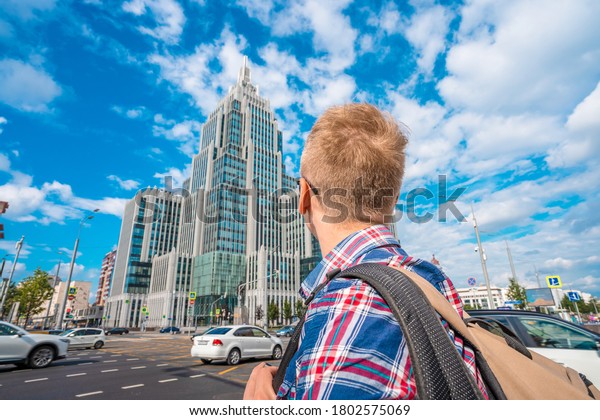 Moscow / Russia - 16 Aug 2020: A young man throws\
back his head and looks at the modern high-rise building.\
Multifunctional complex\
Armory