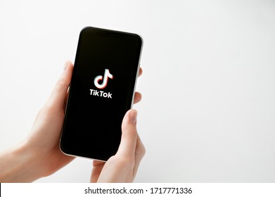 Moscow, Russia, 28 April, 2020. Tik Tok Application Logo On Black Screen Of Iphone X On White Backdrop. Tiktok Social Media Network. Tik Tok App Icon On Smartphone Display. Female Hands Keeps A Phone