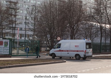 Moscow, Russia – April 13 2021: An Ambulance Drove Up To The Opening Mechanical Gate Of The Hospital. Two Passers-by With Protective Masks On. Translation: Ambulance. Hospital Information Stand