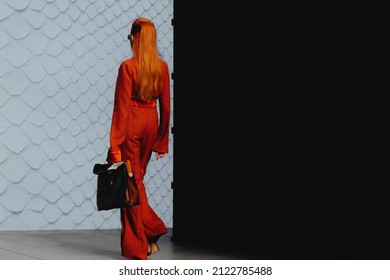 MOSCOW RUSSIA - April 20 2021: Slim red-haired fashion model dressed in a red stylish suit and holding black bag walking the runway