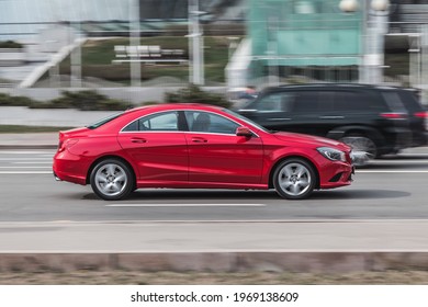 Moscow , Russia - April 2021: Side view rolling shot with red car in motion. Mercedes CLA Class driving along the street in city with blurred background