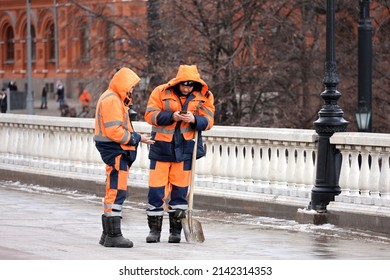 Moscow, Russia - April 2022: Worker With Shovel Standing With Smartphone On Manezh Square And Talking With Friend. Street Cleaning, Snow Removal  In Spring City