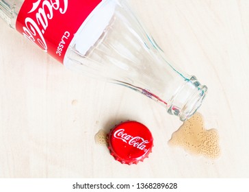 MOSCOW, RUSSIA - APRIL 4, 2019: Red Crown Cap, Empty Bottle From Coca-Cola Beverage And Spilled Puddle On Wooden Table. Coca-Cola (Coke) Is Carbonated Soft Drink Manufactured By The Coca-Cola Company