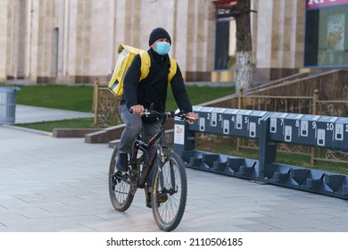 Moscow, Russia - April 4, 2020: Spring City. Photography Of Delivery Man At The Street Within Day Time. Cycling. Frontal View During Coronavirus Pandemic. He Wear, Use Surgical Mask. Yandex Eda