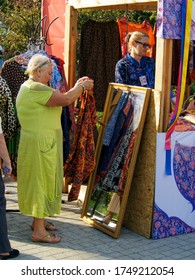 Moscow, Russia - Aug 21, 2016: An Older Woman Looks At A Dress For Trying On At A Street Stall With Clothes