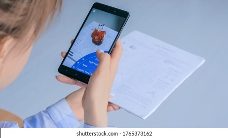 MOSCOW, RUSSIA - AUGUST 1, 2019. Woman using smartphone with augmented reality app - 3d anatomical model of human heart. Future, AR, medical, anatomy, technology, healthcare, cardiology concept