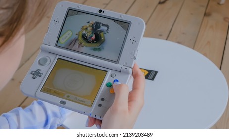 MOSCOW, RUSSIA - AUGUST 1, 2019. Woman gamer hand using grey handheld game console Nintendo 3ds and playing with augmented reality application - close up view. Gaming, AR and technology concept