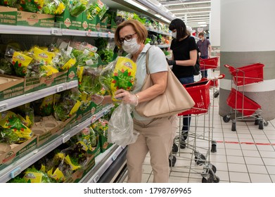 Moscow, Russia, August 2020: Senior Woman In A Mask, Glasses And Gloves Selects Greens In A Grocery Shop. In The Background - Shopping Carts And Other Customers With Masks