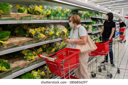 Moscow, Russia, August 2020: Senior Woman In A Mask And Gloves Selects Greens In A Grocery Shop. In The Background - Shopping Carts And Other Customers With Masks 