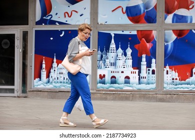 Moscow, Russia - August 2022: Surprised Woman With Smartphone Walking On City Street On Background Of Wall Decorated For The Birthday Of Moscow