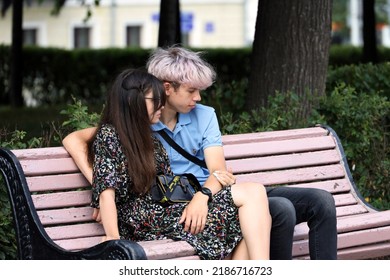 Moscow, Russia - August 2022: Teen Couple In Love  Sitting On A Street Bench. City Life In Summer, Guy With Pink Dyed Hair Embracing Girl In Sunglasses