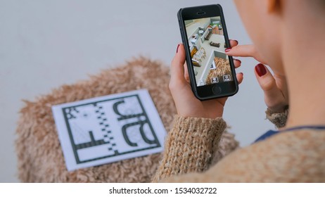 MOSCOW, RUSSIA - AUGUST 29, 2018. Woman using smartphone with augmented reality app and checking virtual house plan. Future and technology concept
