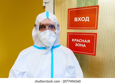 MOSCOW, RUSSIA - CIRCA NOVEMBER 2020: PORTRAIT OF A TIRED (WEARED-OUT) DOCTOR IN A PROTECTIVE SUIT IN THE BACKGROUND OF THE DOOR WITH THE INSCRIPTION IN RUSSIAN "ENTRANCE - RED ZONE" COVID-19 pandemic