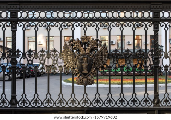 Moscow, Russia - December 01, 2019: Metal coat of\
arms of the Russian Federation on the black fence of the building\
of the Prosecutor\'s Office. Two-headed eagle holds a shield with\
the text Law