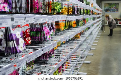 Moscow, Russia, December 2019: Stand with seeds of different varieties of annual flowers: marigold, petunias, etc. On a blurry background-a customer looks at the product and talks on smartphone