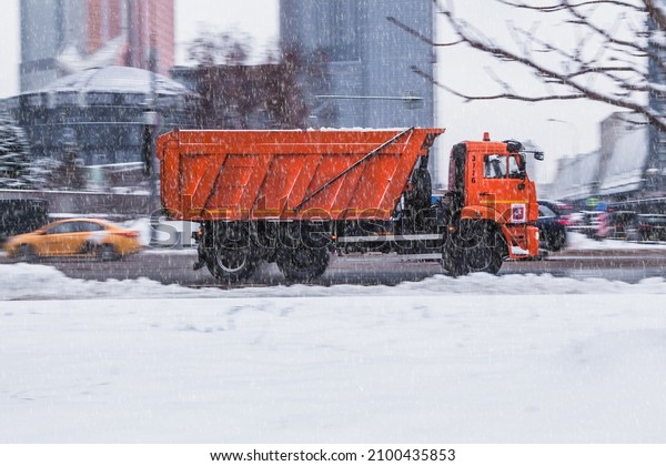 Moscow, Russia - December 2021: Dump\
heavy truck rides on the wet winter road in city. Orange recycling\
truck in motion on snowy city street during\
snowfall