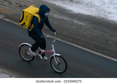 Moscow, Russia, December 8, 2021. Yandex Delivery Courier Rides A Bicycle In A Mask On The Road. Food Delivery In Winter.