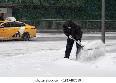 Moscow. Russia. February 12, 2021. A Utility Worker Wearing A Protective Mask Shovels Snow With A Shovel On A City Street During A Snowfall On A Winter Day.