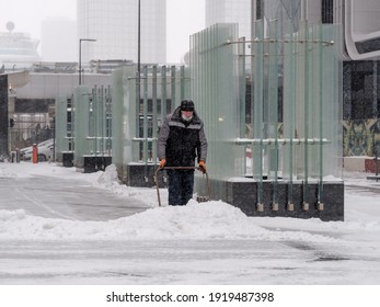 Moscow. Russia. February 12, 2021. A Utility Worker Wearing A Protective Mask Removes Snow With A Scraper On A City Street During A Snowfall On A Winter Day.