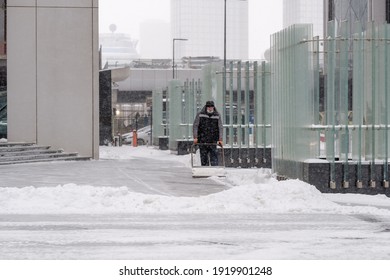 Moscow. Russia. February 12, 2021. A Utility Worker Wearing A Protective Mask Removes Snow With A Scraper On A City Street During A Snowfall On A Winter Day.