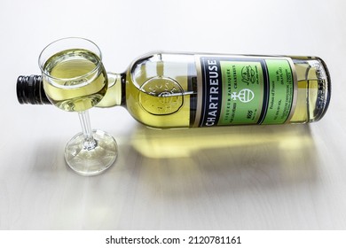 Moscow, Russia - February 3, 2022: Lying Bottle Of Green Chartreuse Liqueur And Liqueur Glass On Pale Table (focus On The Bottle). The Liqueur Has Been Made By The Carthusian Monks N France Since 1737