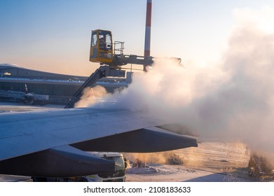 Moscow, Russia - January 12, 2022: International Airport. De-icing an aircraft wing. Process of spraying anti-icing white fluid the rear part of the wing of a plane at the airport at sunrise in winter
