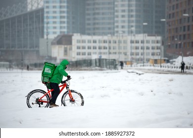 Moscow, Russia - January 2, 2021: Food Delivery Mania Bright Clothes Riding On A Bicycle Through Snow On Winter Day, Moscow