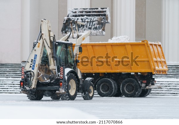 Moscow,
Russia - January 26, 2022: Municipal city service cleans street  in
the public park from white snow after blizzard. Urban industrial
conceptLow angle view. Loading snow onto a
truck