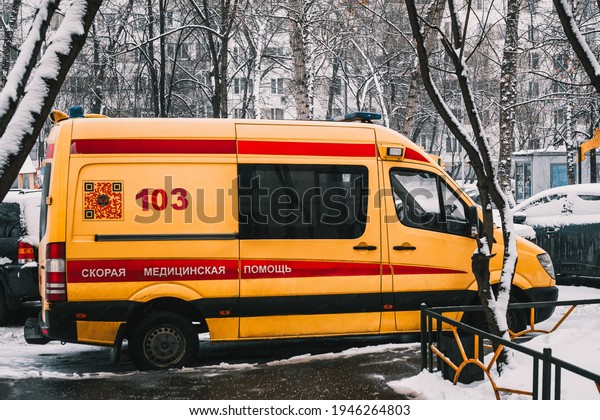 Moscow, Russia - January 28 2021: A yellow\
ambulance is parked in the courtyard of a residential building.\
Side view. Trees, cars nearby and the road is covered with snow.\
Translation: Ambulance