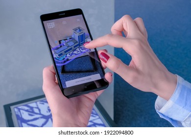 MOSCOW, RUSSIA - JANUARY 5, 2020. Woman using smartphone with augmented reality app and rotating 3d virtual model of modern building skyscraper in room. Future, AR, architecture and technology concept