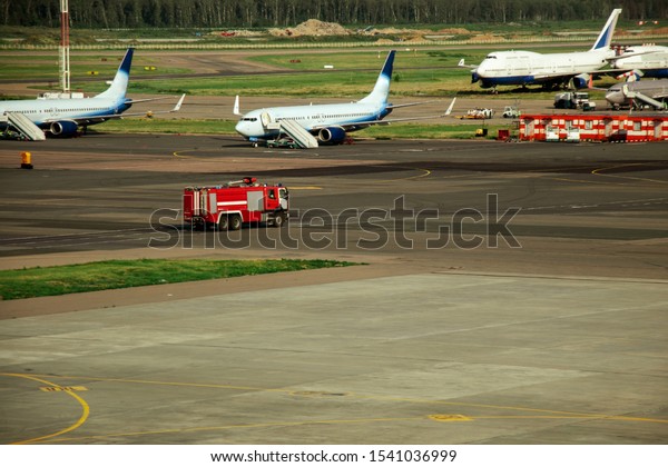 Moscow, Russia - July 01,\
2019: Fire truck on the runway near the aircraft. Airport Rescue\
Service. Firefighters and fire department at the airport. Crisis\
Response System
