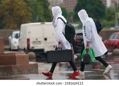 Moscow, Russia - July 10, 2022: Raining Day In City At Summer. Wet Young Man And Woman Put On Rain Coat. Texture Of Strong, Fresh, Powerful Water Drops, Sprays. Young Man Carrying Musical Instrument