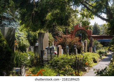 Moscow, Russia - July, 17, 2022. View of the tombstones on the alley of the Novodevichy cemetery. Stone sculptures, funeral flowers, iron fences. Summer sunny day, green trees.