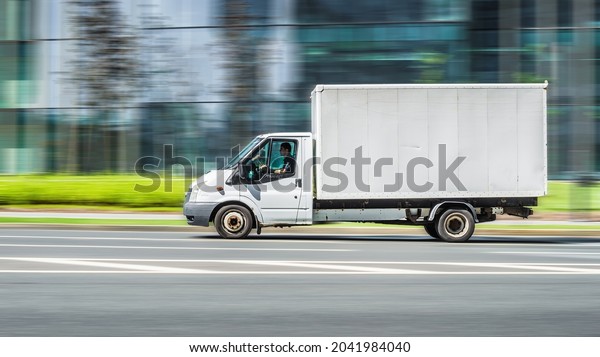 Moscow, Russia - July 2021: Ford Transit cargo box\
van truck in the city street. Side view of white light commercial\
vehicle in motion